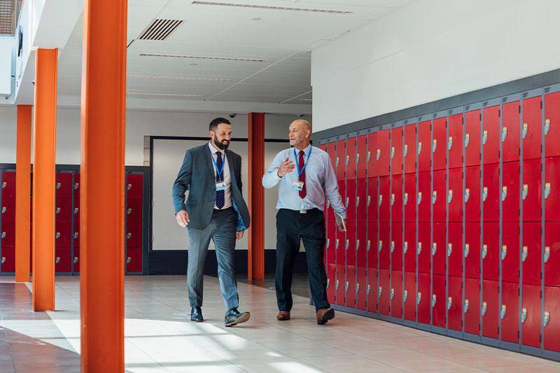 Two school administrators walk and talk by hallway lockers